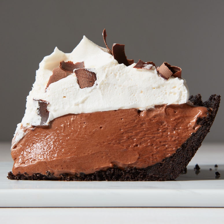 A slice of chocolate filling on a Oreo cookie crust topping with whipped cream and chocolate shavings.
